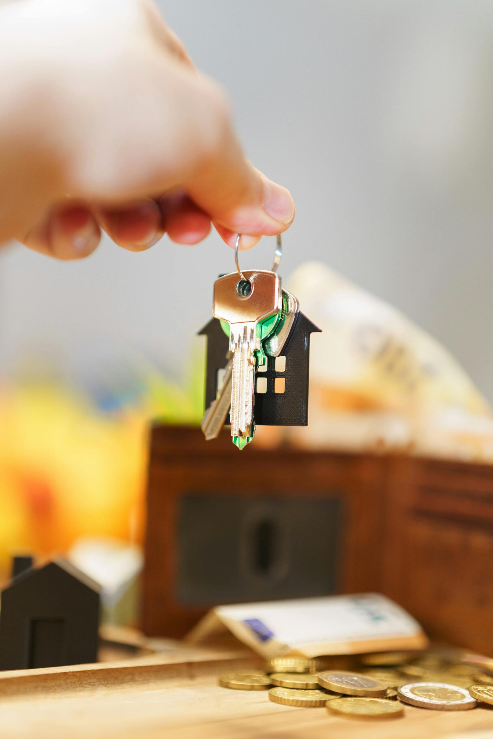 Hand holding house keys representing real estate investment with coins and wallet.